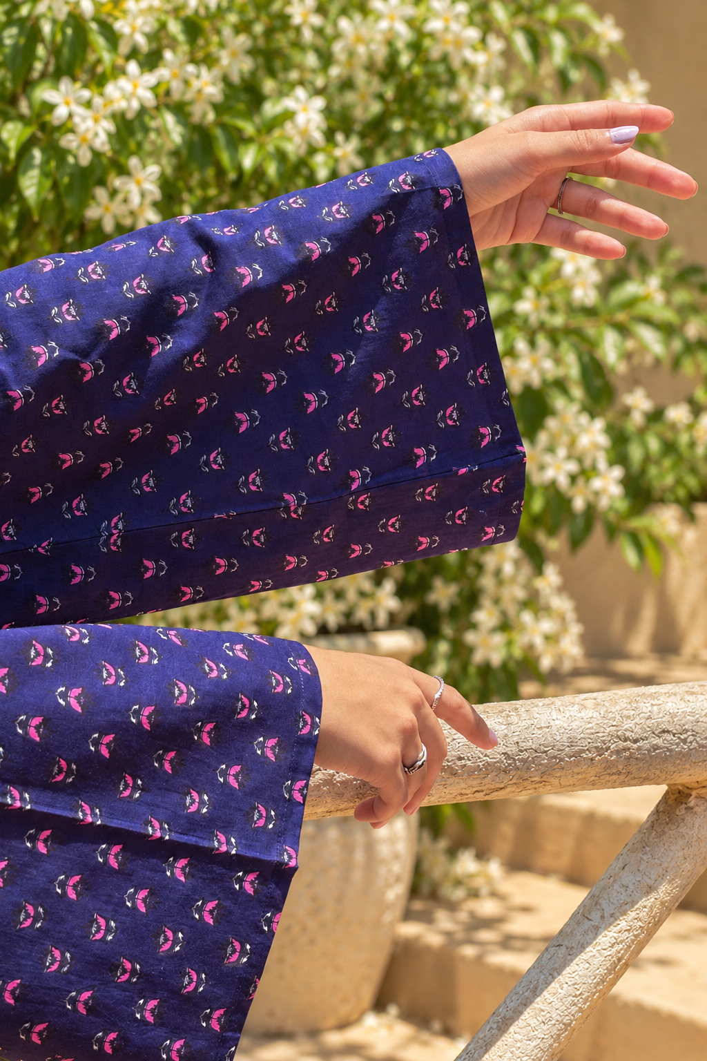 Woman wearing a jiva-blue patterned top standing outdoors with greenery in the background