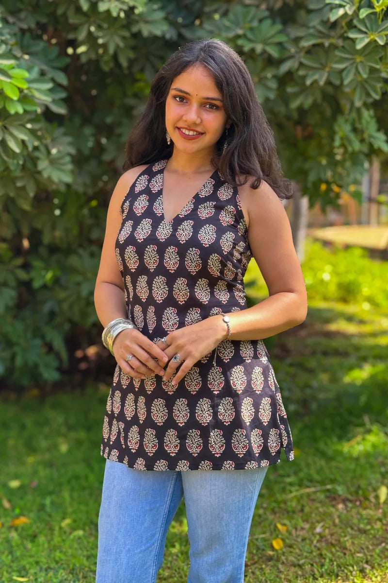 Woman wearing a paisley patterned top and jeans standing outdoors with greenery in the background
