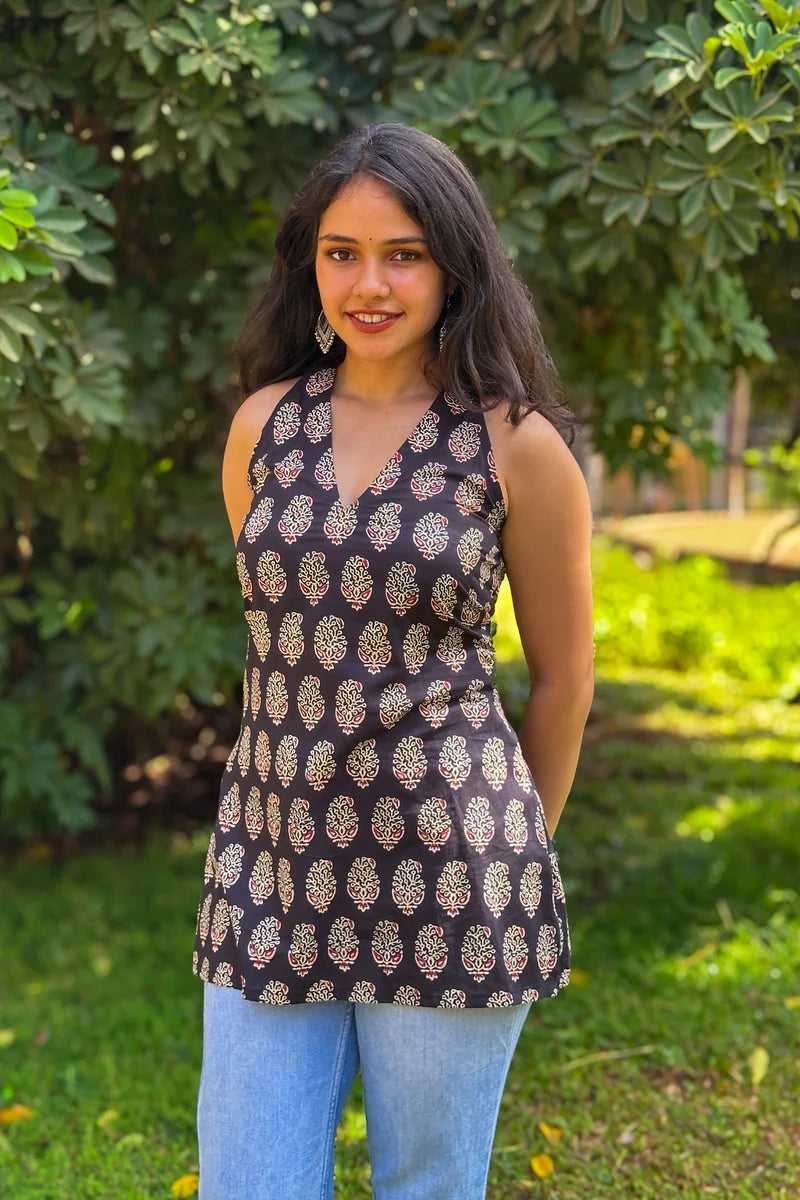 Woman wearing a paisley patterned sleeveless top and jeans standing outdoors with greenery in the background
