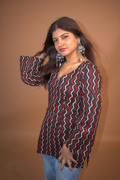 Woman wearing a zigzag patterned top with bell sleeves against a background