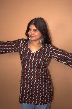 Woman wearing a zigzag patterned top with arms outstretched against a beige background