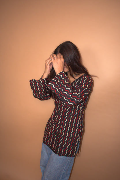 Person wearing a zigzag patterned shirt and jeans against a beige background