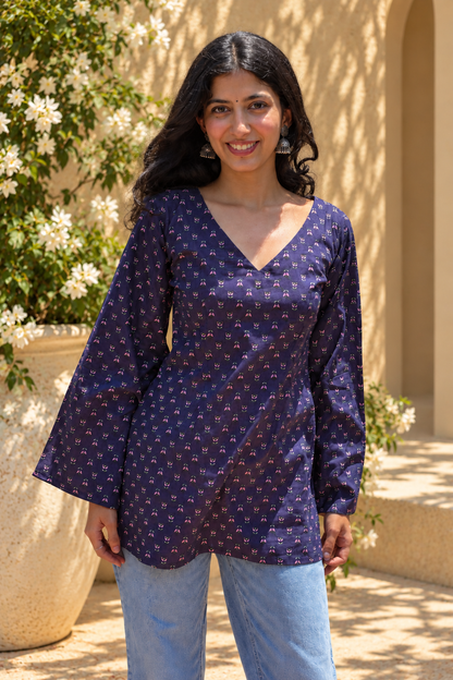 Woman wearing a jiva-blue patterned top standing outdoors with greenery in the background 
