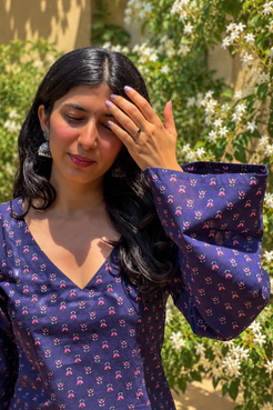 Woman wearing a jiva-blue patterned top standing outdoors with greenery in the background 