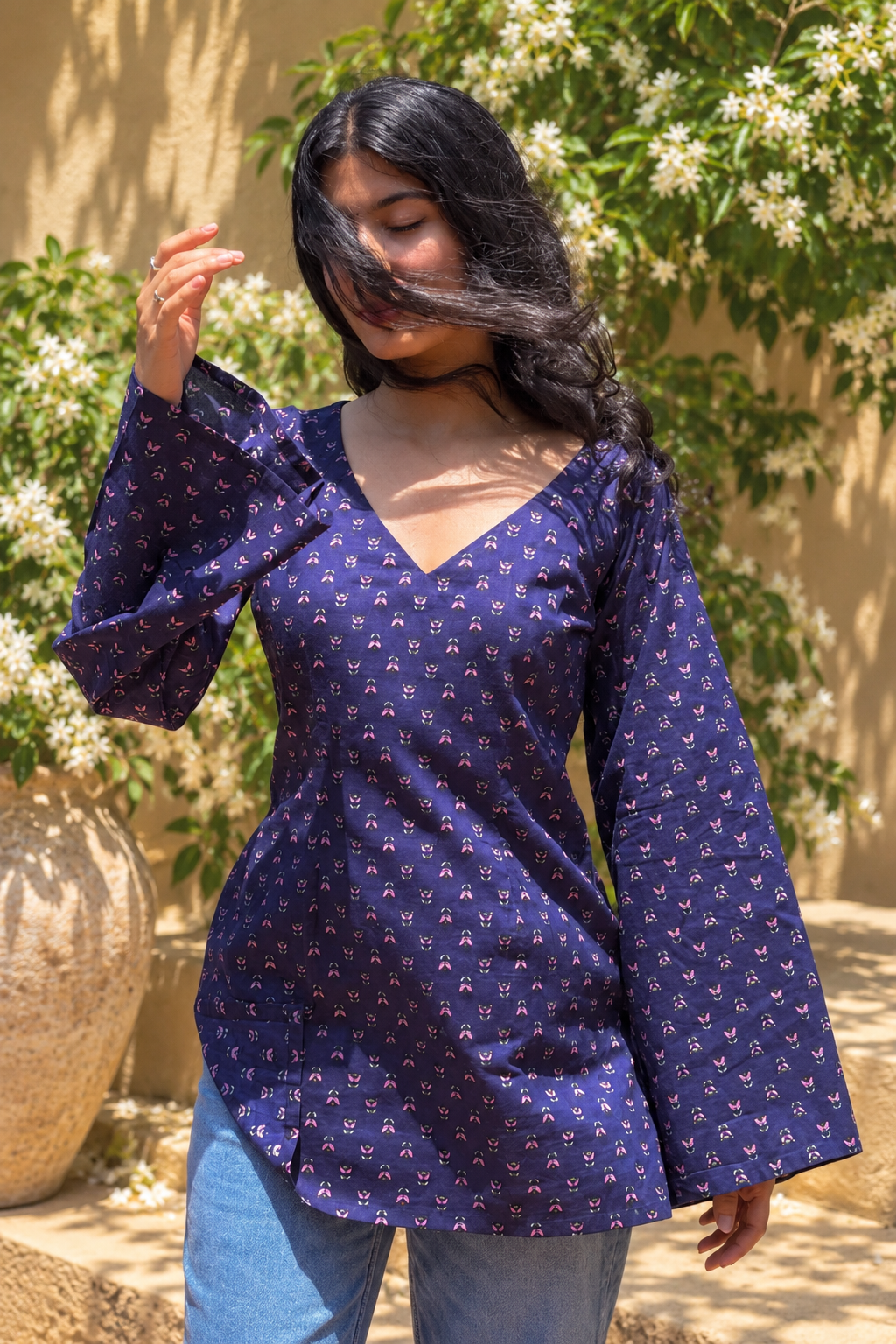 Woman wearing a jiva-blue patterned top standing outdoors with greenery in the background 