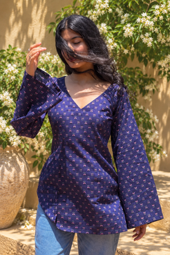 Woman wearing a jiva-blue patterned top standing outdoors with greenery in the background 