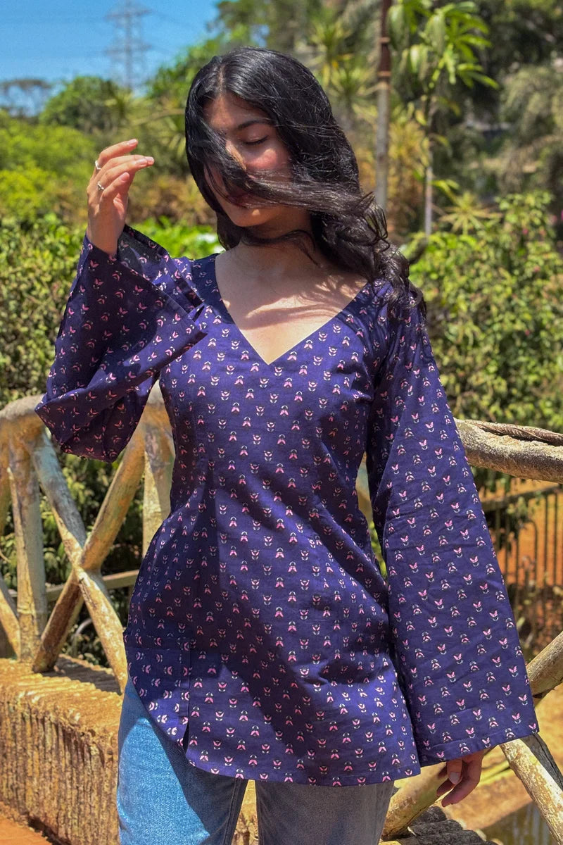 Woman wearing a  jiva-blue patterned top standing outdoors with greenery in the background 