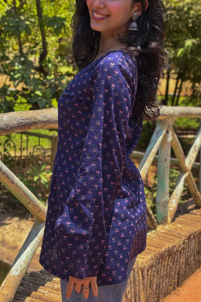 Woman wearing a  jiva-blue patterned top standing outdoors with greenery in the background 