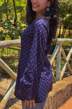 Woman wearing a  jiva-blue patterned top standing outdoors with greenery in the background 