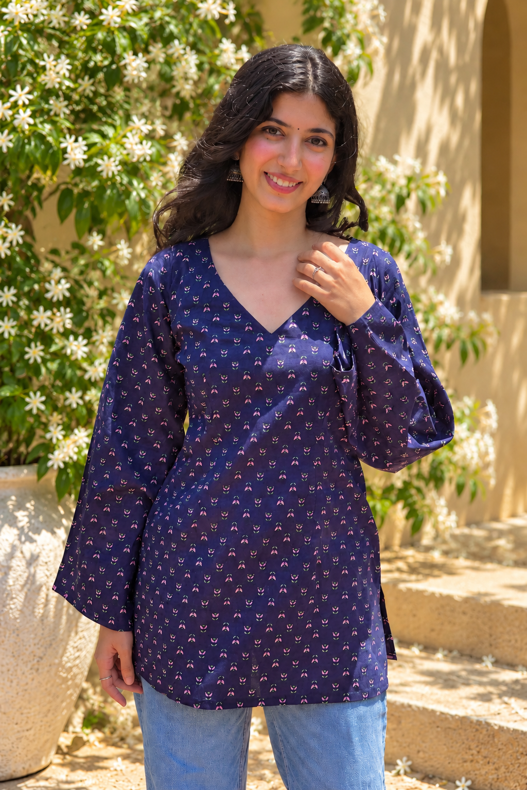 Woman wearing a jiva-blue patterned top standing outdoors with greenery in the background 
