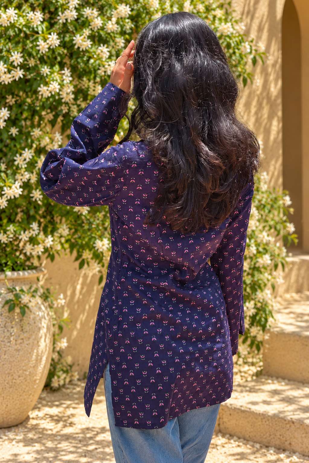 Woman wearing a jiva-blue patterned top standing outdoors with greenery in the background 