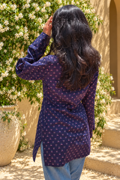 Woman wearing a jiva-blue patterned top standing outdoors with greenery in the background 