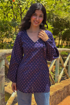 Woman wearing a  jiva-blue patterned top standing on a wooden bridge with greenery in the background 