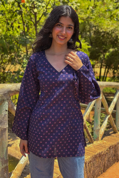 Woman wearing a  jiva-blue patterned top standing on a wooden bridge with greenery in the background 
