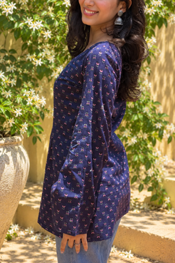 Woman wearing a jiva-blue patterned top standing outdoors with greenery in the background 