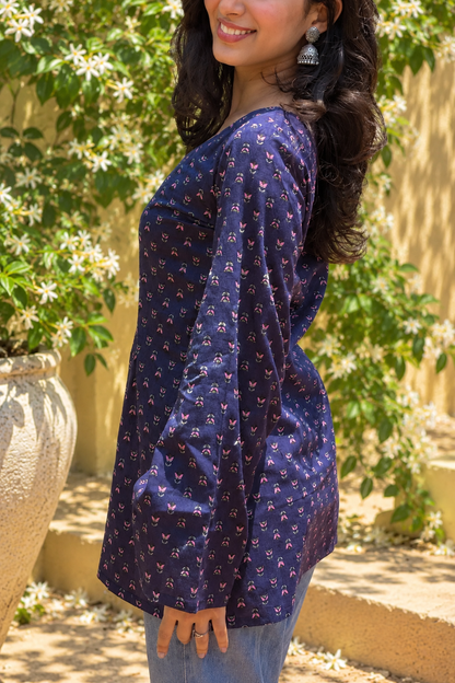 Woman wearing a jiva-blue patterned top standing outdoors with greenery in the background 