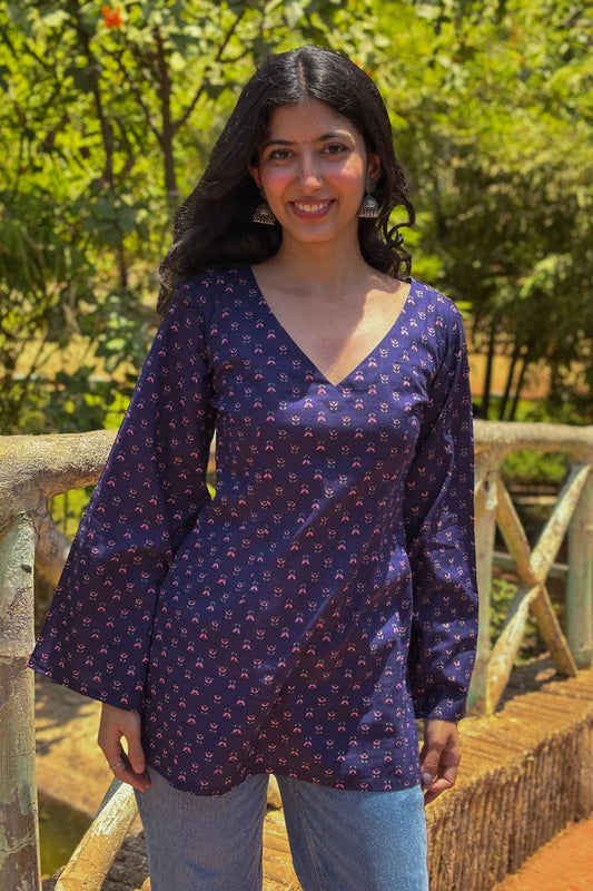 Woman wearing a jiva-blue patterned top standing outdoors with greenery in the background 
