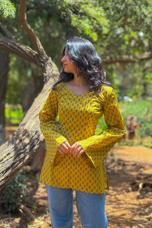 Woman in a jiva-yellow patterned top standing outdoors with trees in the background