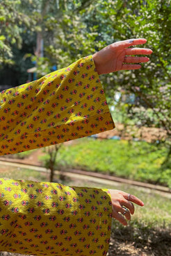 Person wearing a jiva-yellow floral dress with greenery in the background