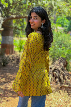 Woman wearing a jiva-yellow patterned top outdoors with greenery in the background