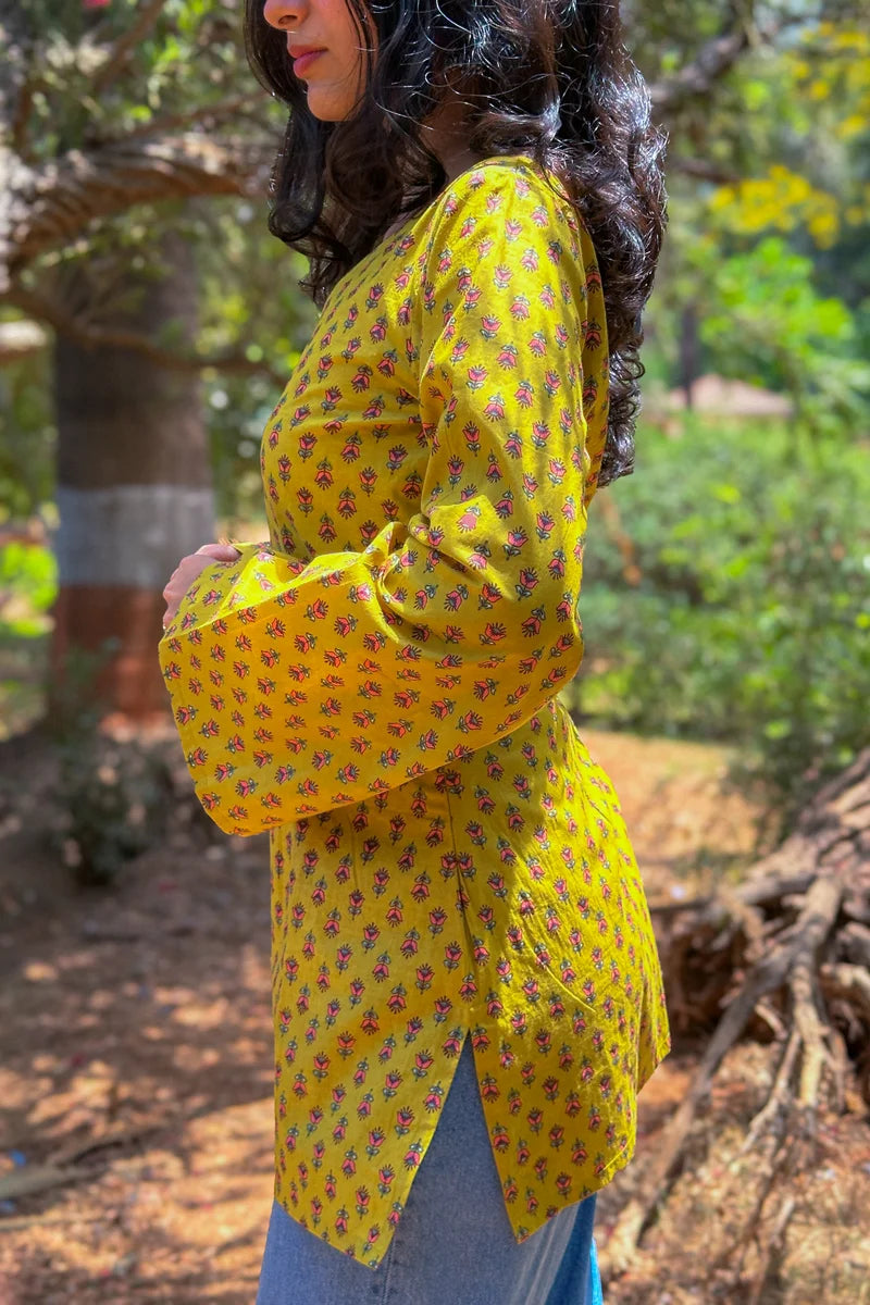 Woman wearing a jiva-yellow floral blouse outdoors with greenery in the background