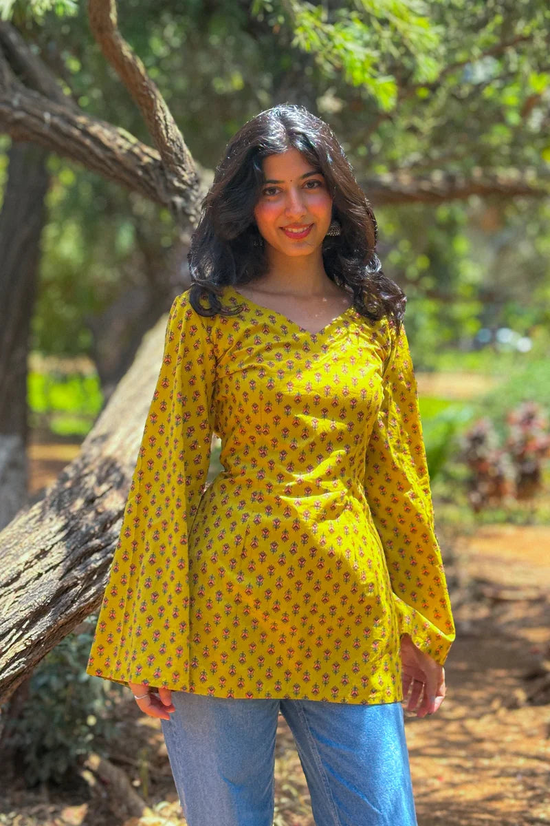 Woman in a jiva-yellow patterned top standing outdoors with greenery in the background