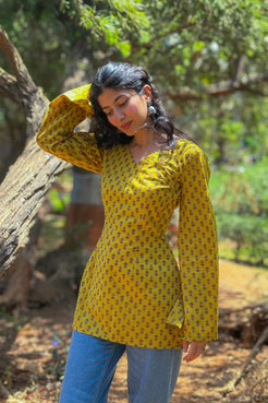 Woman wearing a jiva-yellow patterned top outdoors with greenery in the background