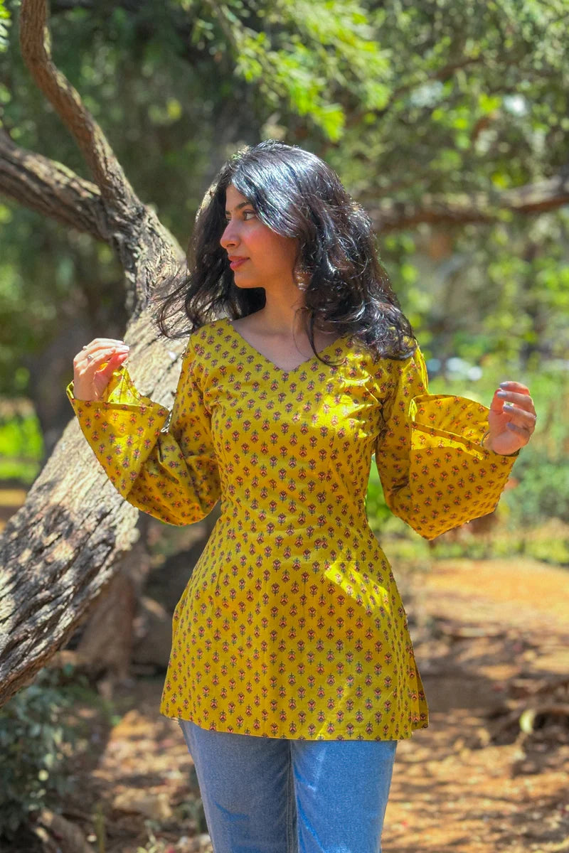 Woman wearing a jiva-yellow patterned top standing outdoors near a tree