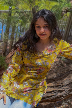 Woman in a jal-yellow floral dress sitting on a wooden log outdoors