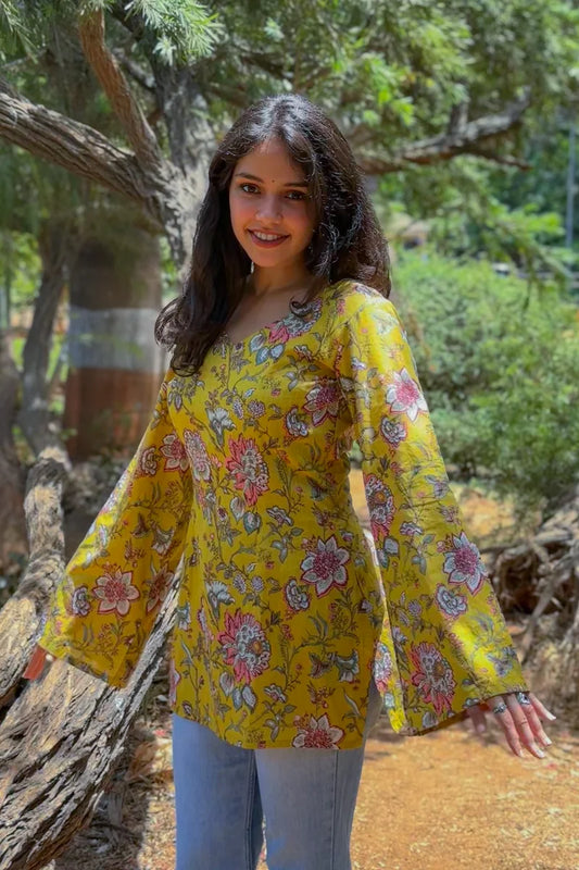 Woman wearing a jal-yellow floral blouse standing outdoors with trees in the background
