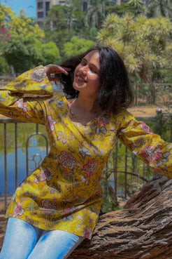 Woman in a jal-yellow floral top sitting on a tree stump with a scenic background