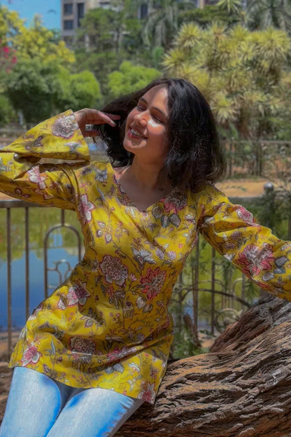 Woman in a jal-yellow floral top sitting on a tree stump with a scenic background