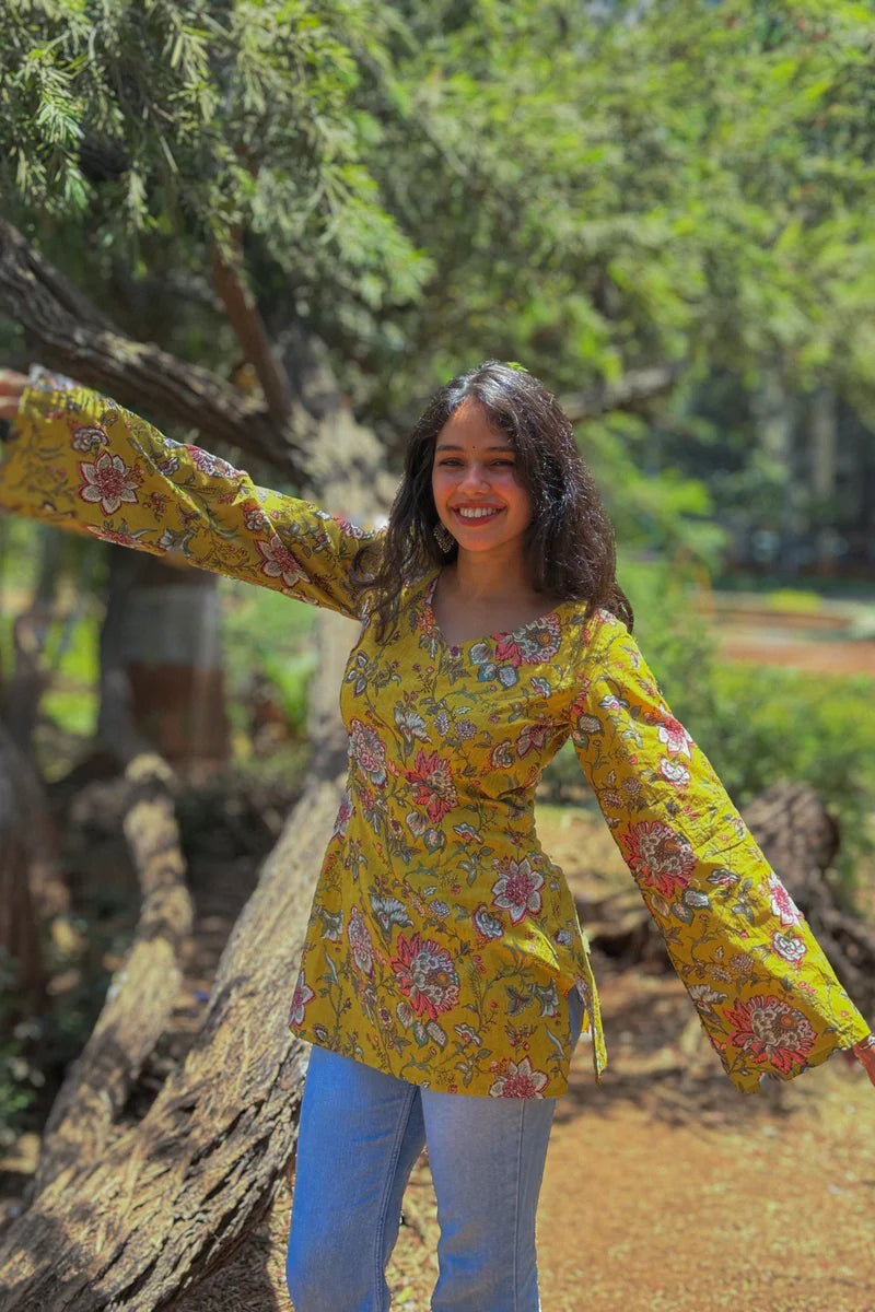 Woman in a jal-yellow floral blouse standing outdoors with greenery in the background