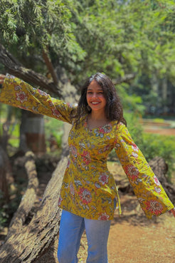 Woman in a jal-yellow floral blouse standing outdoors with greenery in the background