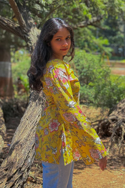 Woman in a jal-yellow floral blouse standing outdoors near a tree