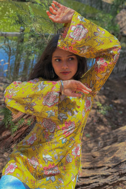 Woman in a jal-yellow floral dress sitting outdoors with greenery in the background