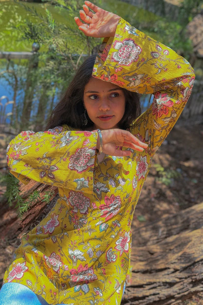 Woman in a jal-yellow floral dress sitting outdoors with greenery in the background