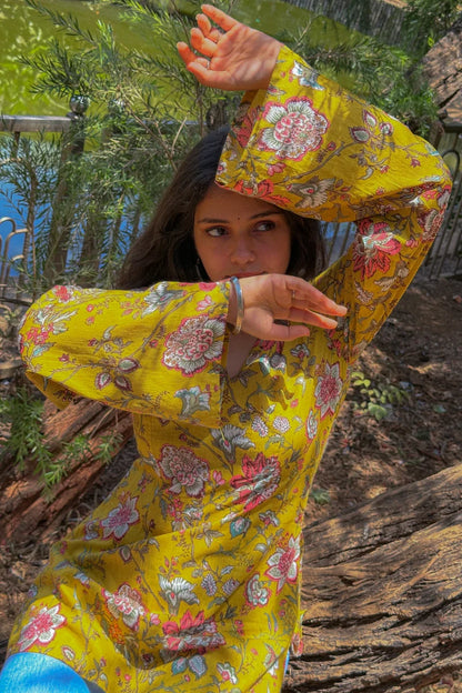 Person wearing a bright jal-yellow floral dress sitting outdoors with greenery in the background
