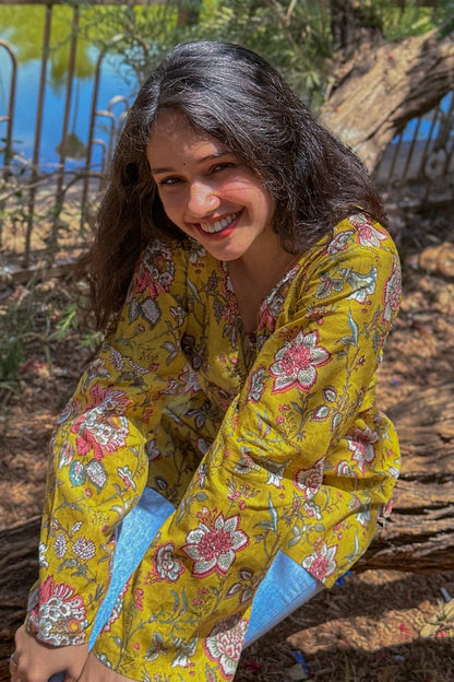 Woman in a jal-yellow floral dress sitting outdoors by a body of water.