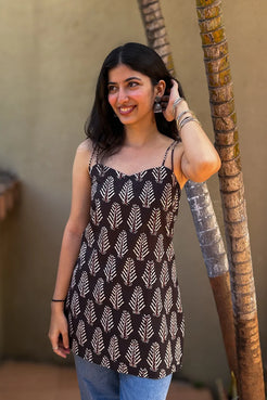 Woman wearing a leaf patterned top with jeans, standing next to a palm tree.