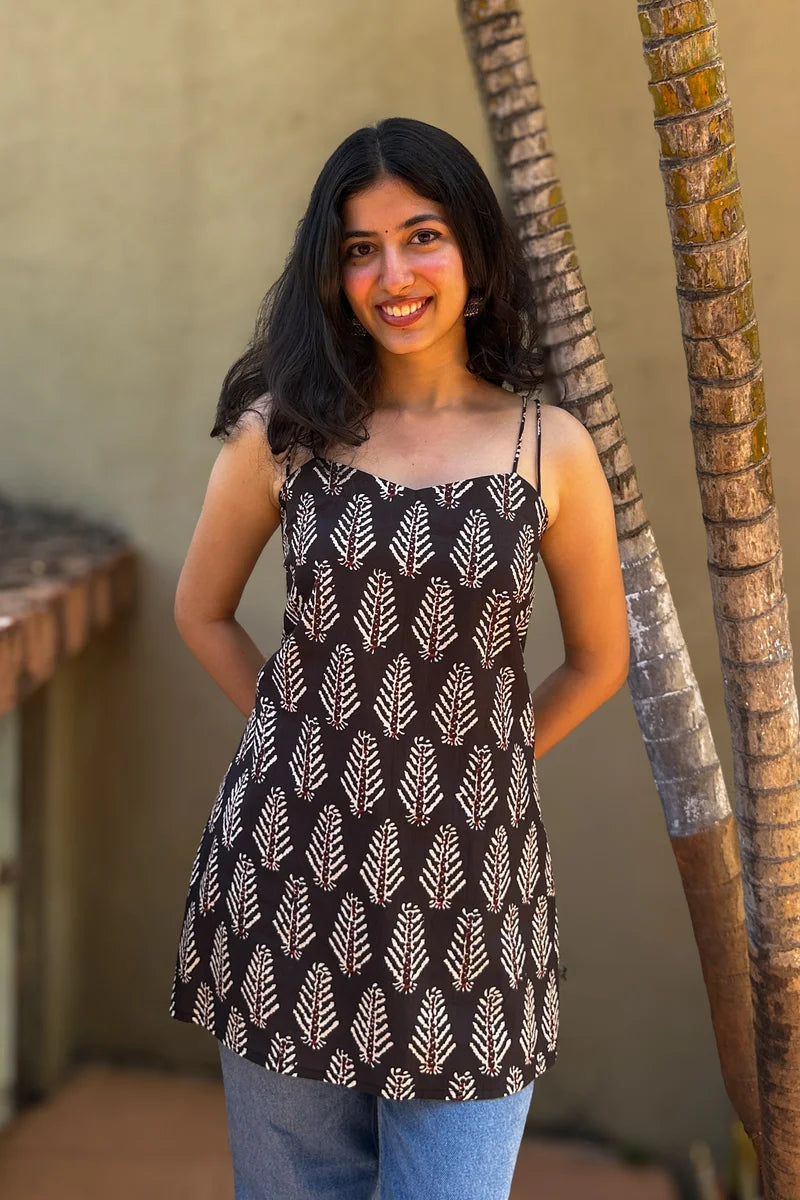 Woman wearing a leaf patterned top and jeans standing next to palm trees.