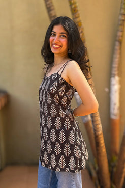 Woman wearing a leaf patterned top with blue jeans, standing against a beige wall.