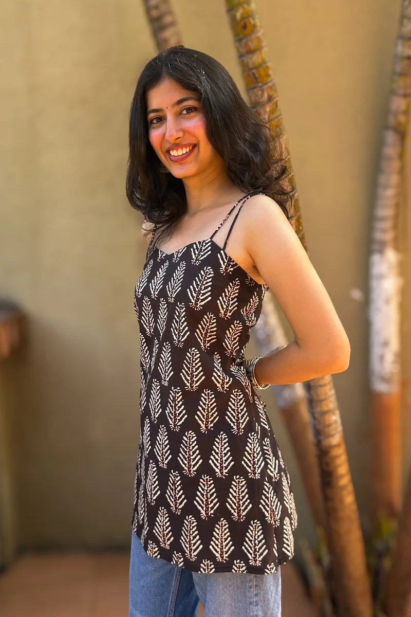 Woman wearing a leaf patterned top with blue jeans, standing against a beige wall.