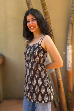 Woman wearing a leaf patterned top with blue jeans, standing against a beige wall.