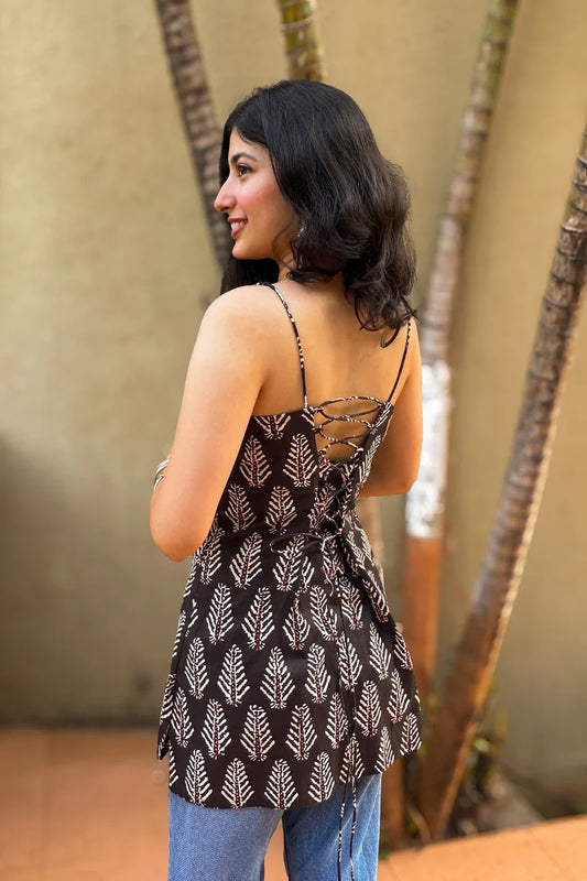 Woman wearing a leaf patterned top with thin straps, standing against a blurred natural background.