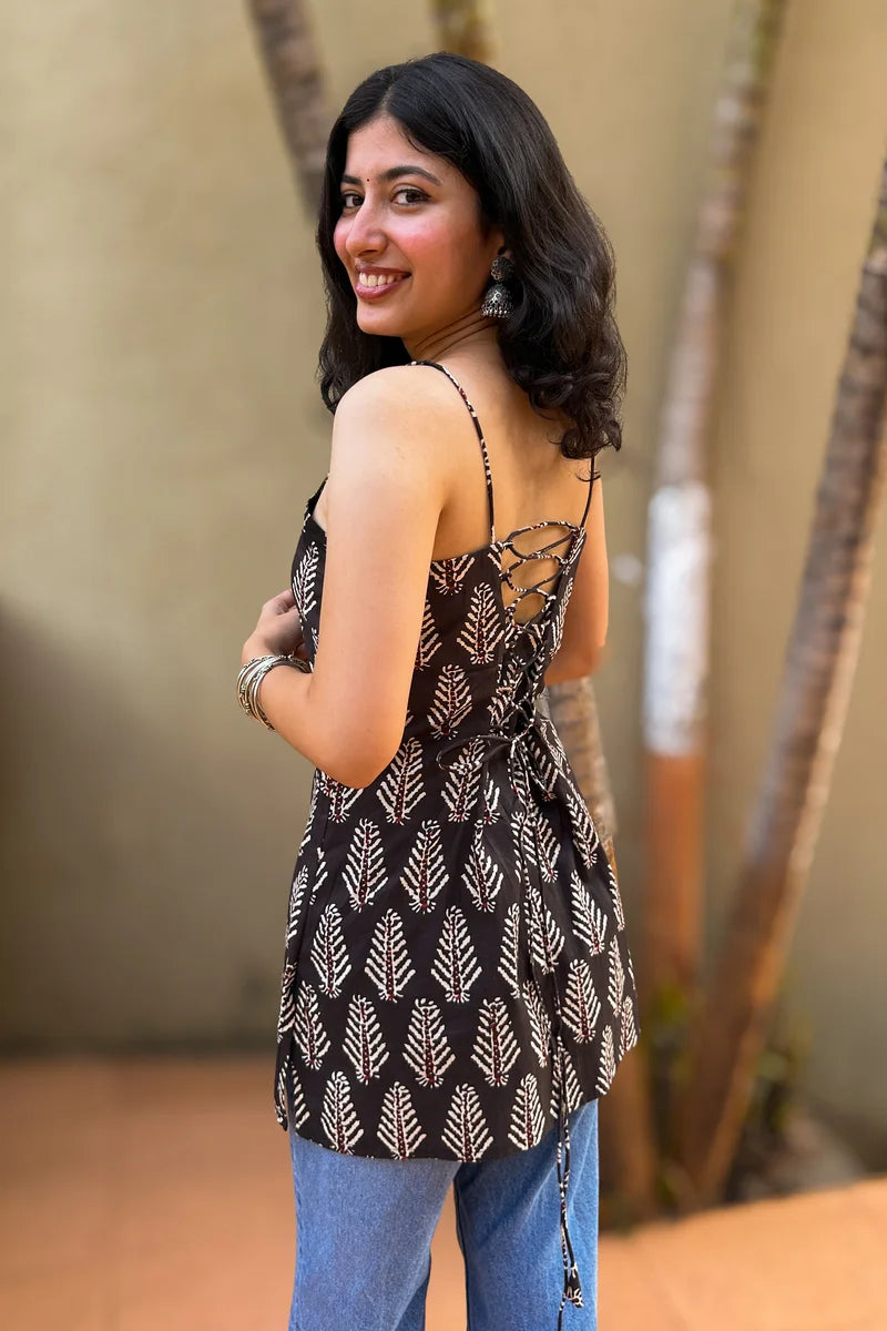 Woman wearing a leaf patterned top and blue jeans standing outdoors with a blurred background