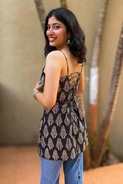 Woman wearing a leaf patterned top and blue jeans standing outdoors with a blurred background
