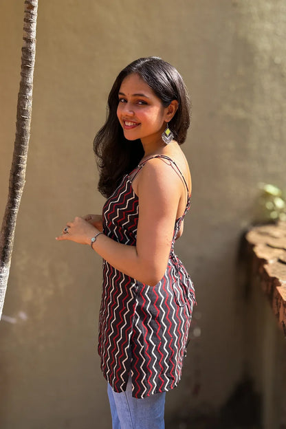 Woman in a zigzag patterned dress standing against a beige wall with a plant to her left.