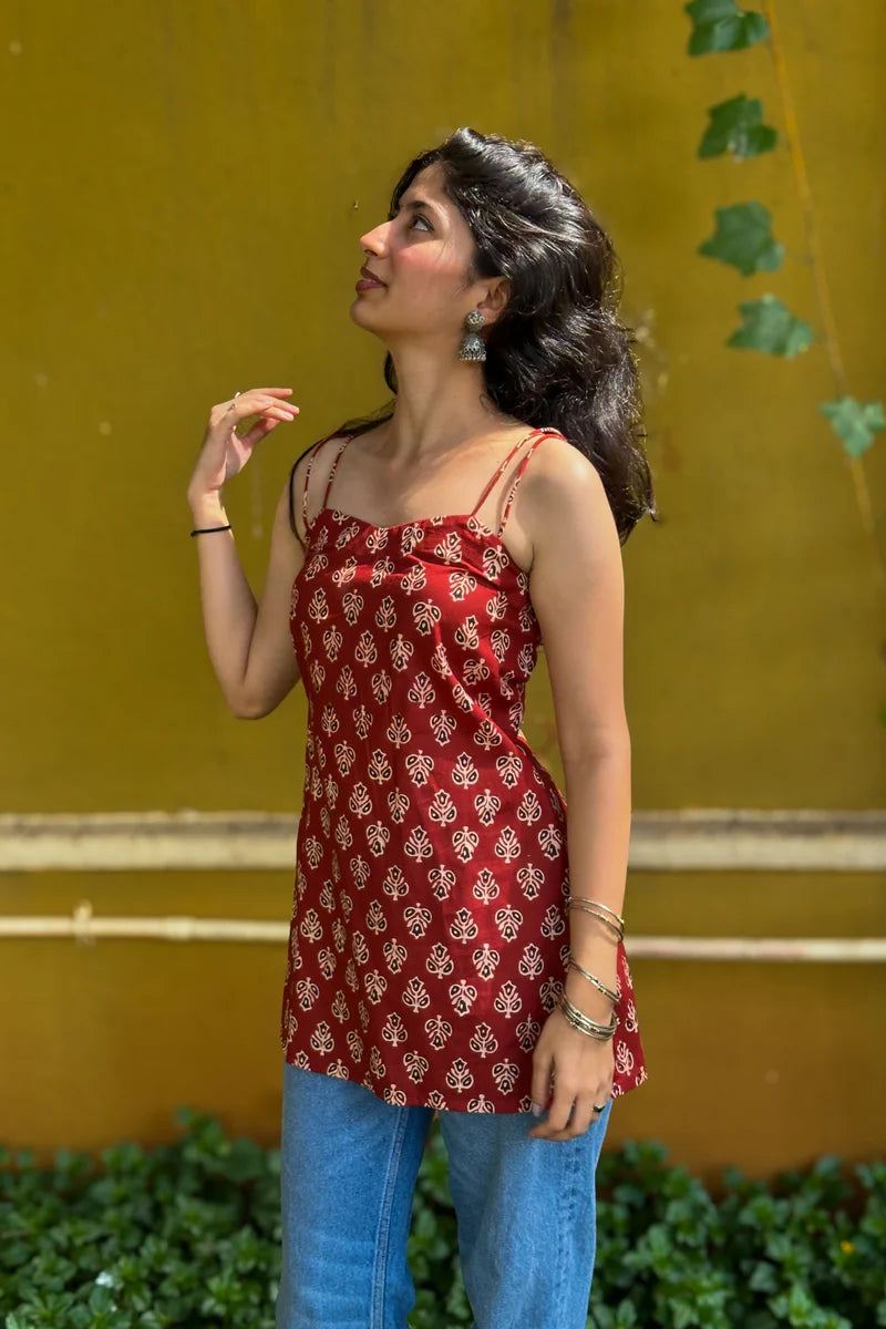 Woman wearing a butta red top and jeans against a wall.