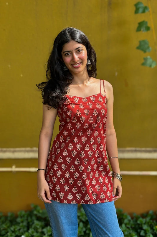 Woman wearing a butta red patterned top and jeans against a wall.